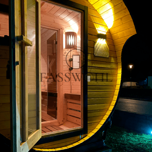 Ein beleuchtetes Fasswohl Saunafass steht mit offener Tür im Garten
